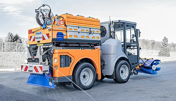 Ein Citymaster ausgestattet mit einer Solesprühanlage steht auf einer Asphaltstraße. Er hat einen Kehrbesen an der Vorderseite. Auf dem Fahrzeug befinden sich gelbe und rote Warnmarkierungen und ist bereit für den Winterdiensteinsatz.