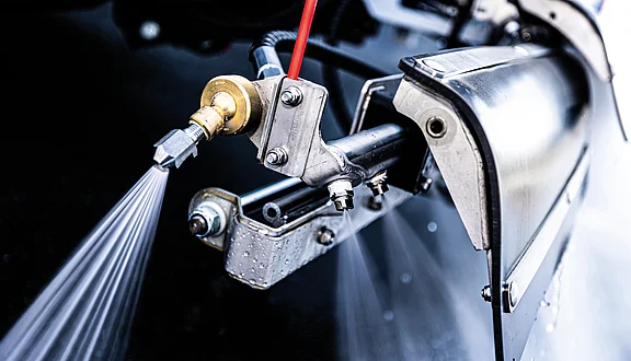 Das Bild zeigt einen Schwemmbalken mit einer Seitendüse im Einsatz. Das Wasser wird mit starkem Druck aus den Düse gebracht, wodurch dreieckige Wasserstrahlen entstehen. Die technische Konstruktion ist aus Edelstahl und robust.