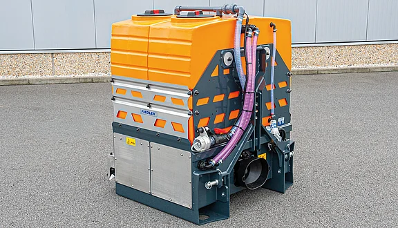 Ein Tanksystem mit verschiedenen Schläuchen und Pumpen steht auf einem asphaltierten Untergrund. Der Tank hat eine rechteckige Form und ist mit Sicherheitsmerkmalen wie Reflexelementen ausgestattet. Die Montage- und Auslassanschlüsse sind deutlich sichtbar.