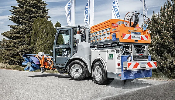 Winterdienst-Fahrzeug Citymaster ZE mit Fiedler-Anbauteilen: Vollelektrische Kehrmaschine mit Frontbesen und Heck-Solesprüher für den Wintereinsatz auf der Straße.