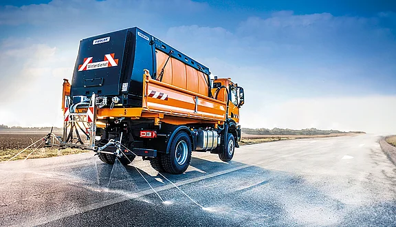 Winterdienst-LKW Mercedes-Benz Atego mit Fiedler Solesprühanlage: Professionelle Soleausbringung zur Glatteisprävention auf einer Landstraße bei winterlichen Verhältnissen.